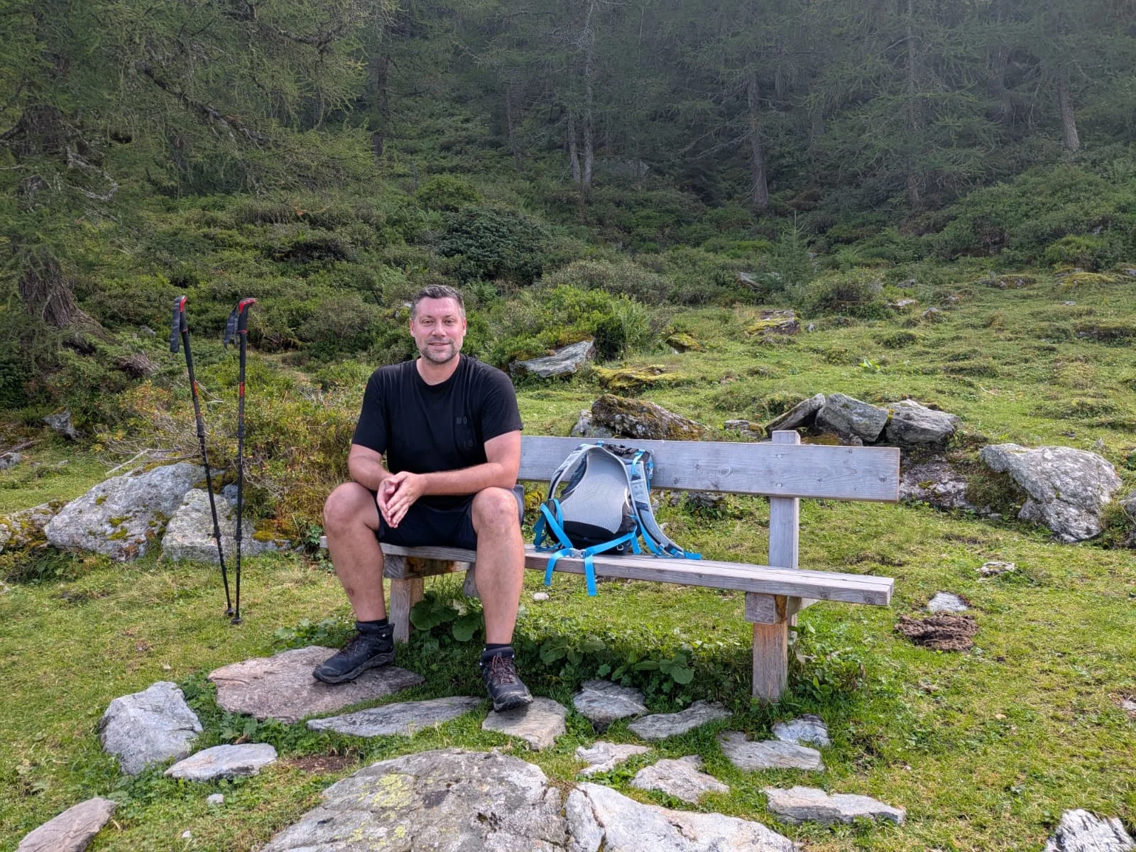 Lukáš Fiedler odpočívá na lavičce při horské túře, vedle má batoh a turistické hole